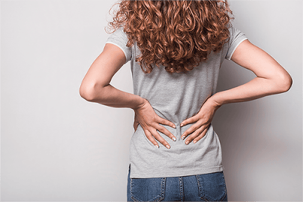 Mujer de espaldas se agarra la parte baja de la espalda debido al dolor referido visceral